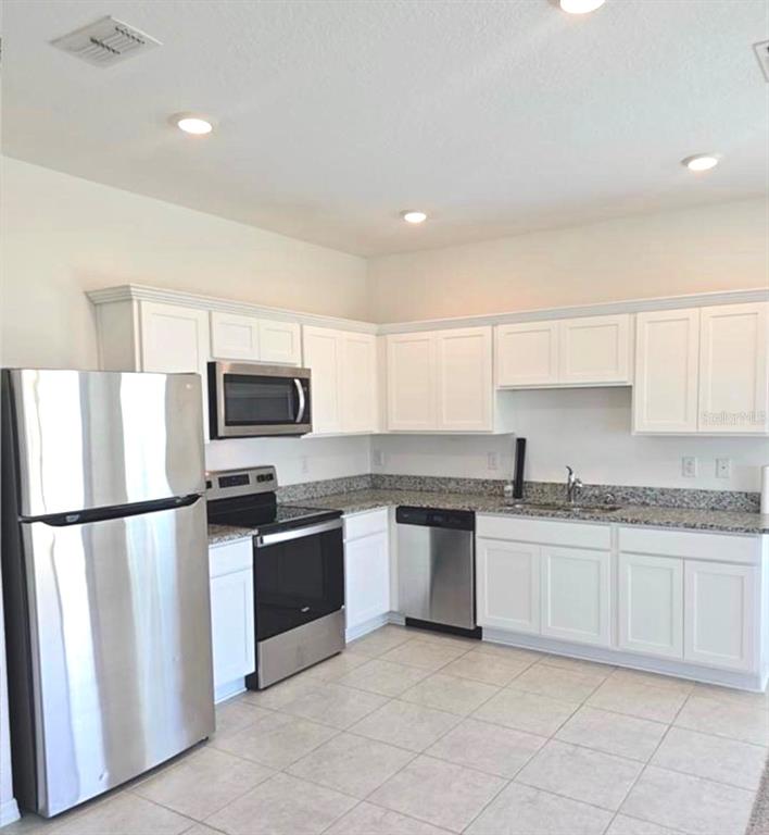 A kitchen features white cabinets, stainless steel appliances, and granite countertops with tile flooring — 1128 MERRILL STREET, DAVENPORT, FL