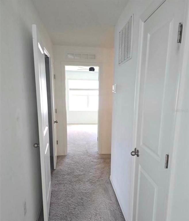A hallway with carpeted flooring leads toward a bright room with a window — 1128 MERRILL STREET, DAVENPORT, FL