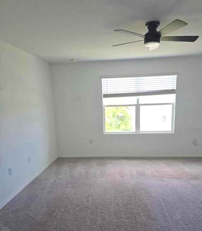 An empty bedroom features beige carpeting, white walls, a ceiling fan, and a window — 1128 MERRILL STREET, DAVENPORT, FL