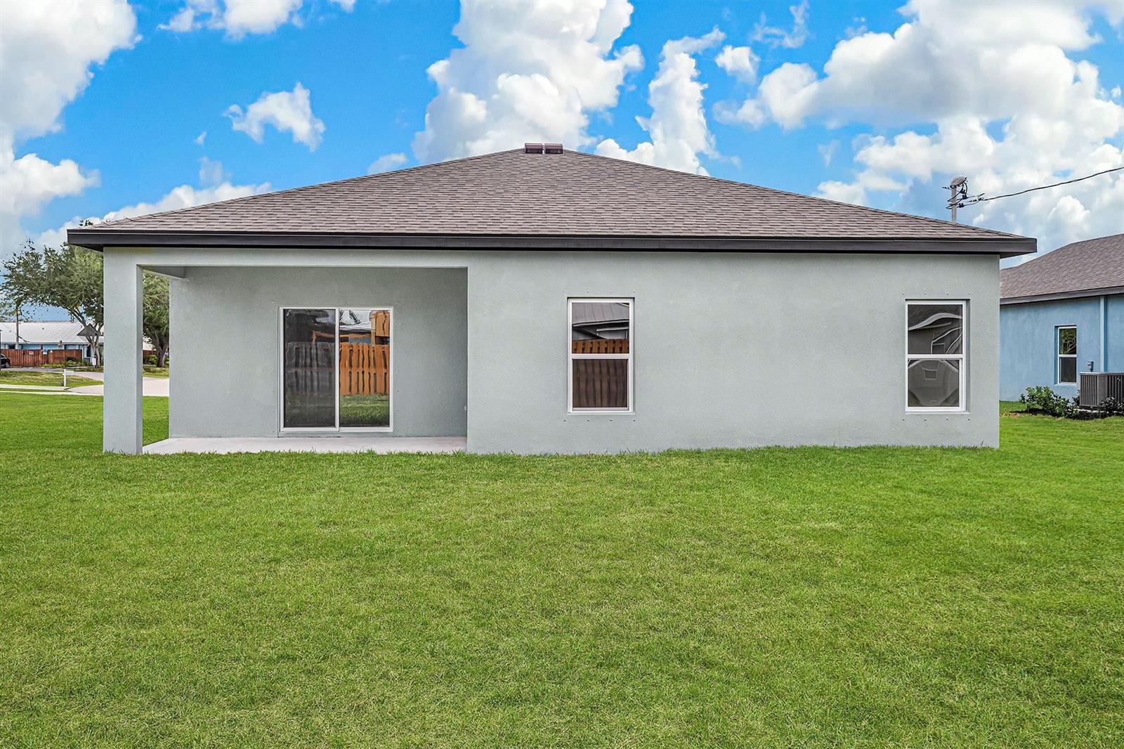 The rear exterior of a single-story house features a covered patio and a grassy yard — 8416 100th Avenue, Vero Beach FL 32967, VERO BEACH, FL