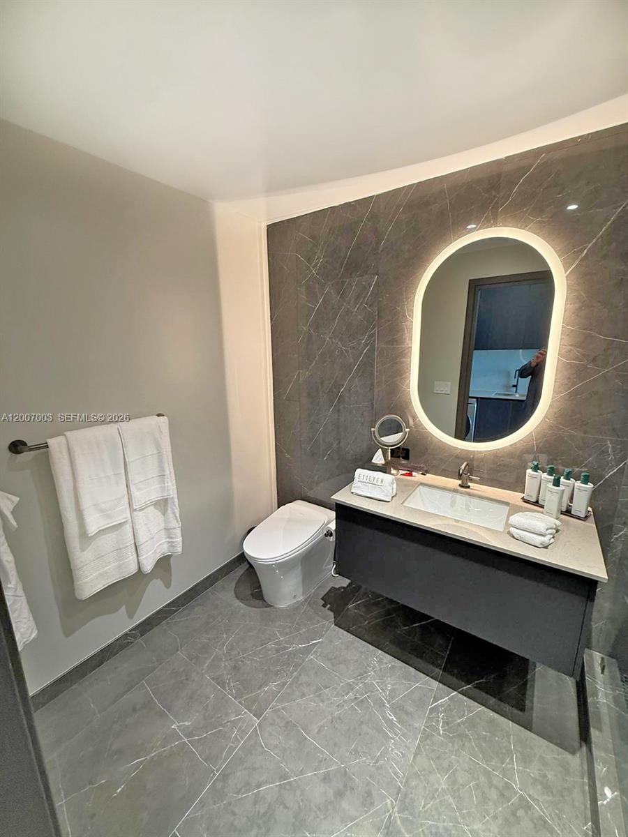 A modern bathroom features a floating vanity, a backlit oval mirror, and gray marble tiling — 20 NE 11th St # 4202, Miami FL 33132, MIAMI, FL
