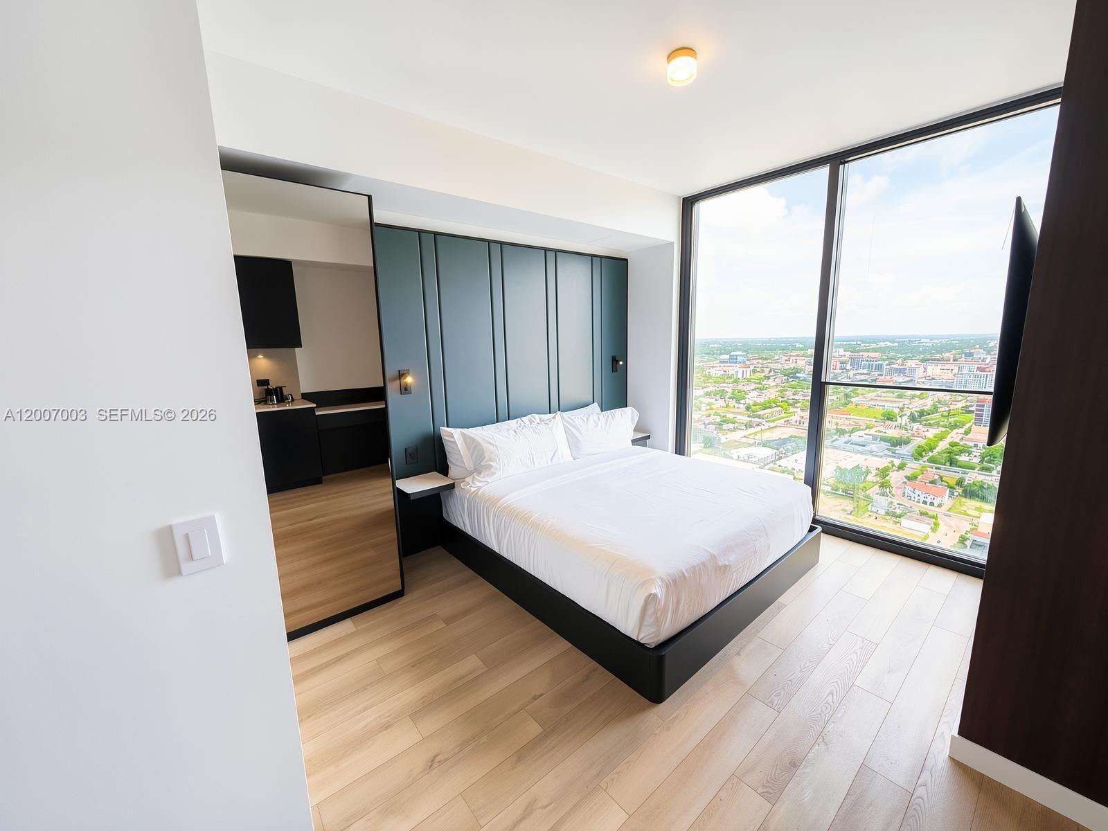 A modern bedroom features a dark blue paneled headboard, a platform bed, and floor-to-ceiling windows — 20 NE 11th St # 4202, Miami FL 33132, MIAMI, FL