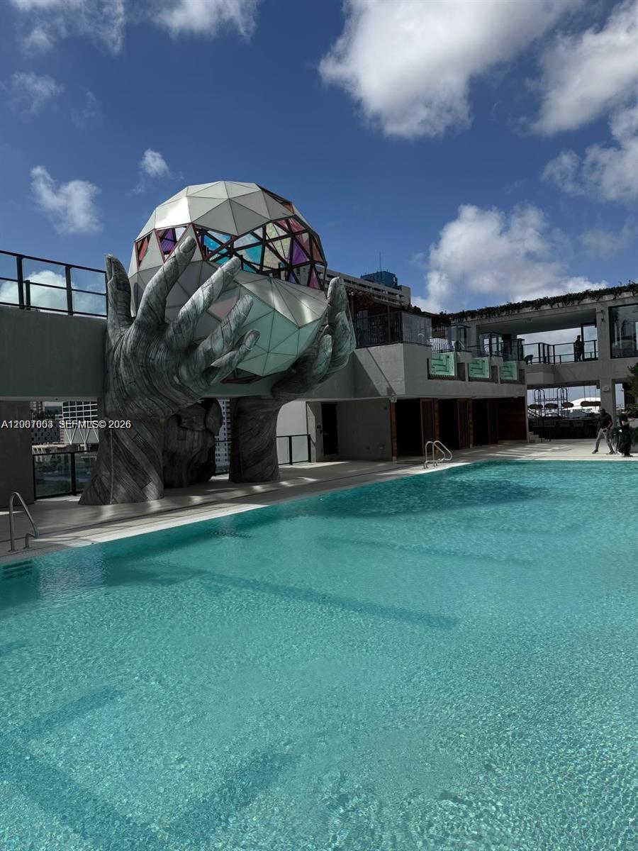 A swimming pool sits in front of a large sculpture of hands holding a geometric sphere — 20 NE 11th St # 4202, Miami FL 33132, MIAMI, FL