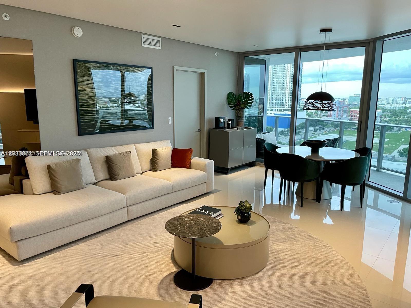 A modern living and dining area features a beige sofa, round coffee table, and floor-to-ceiling windows — 488 NE 18th St # 1901, Miami FL 33132, MIAMI, FL
