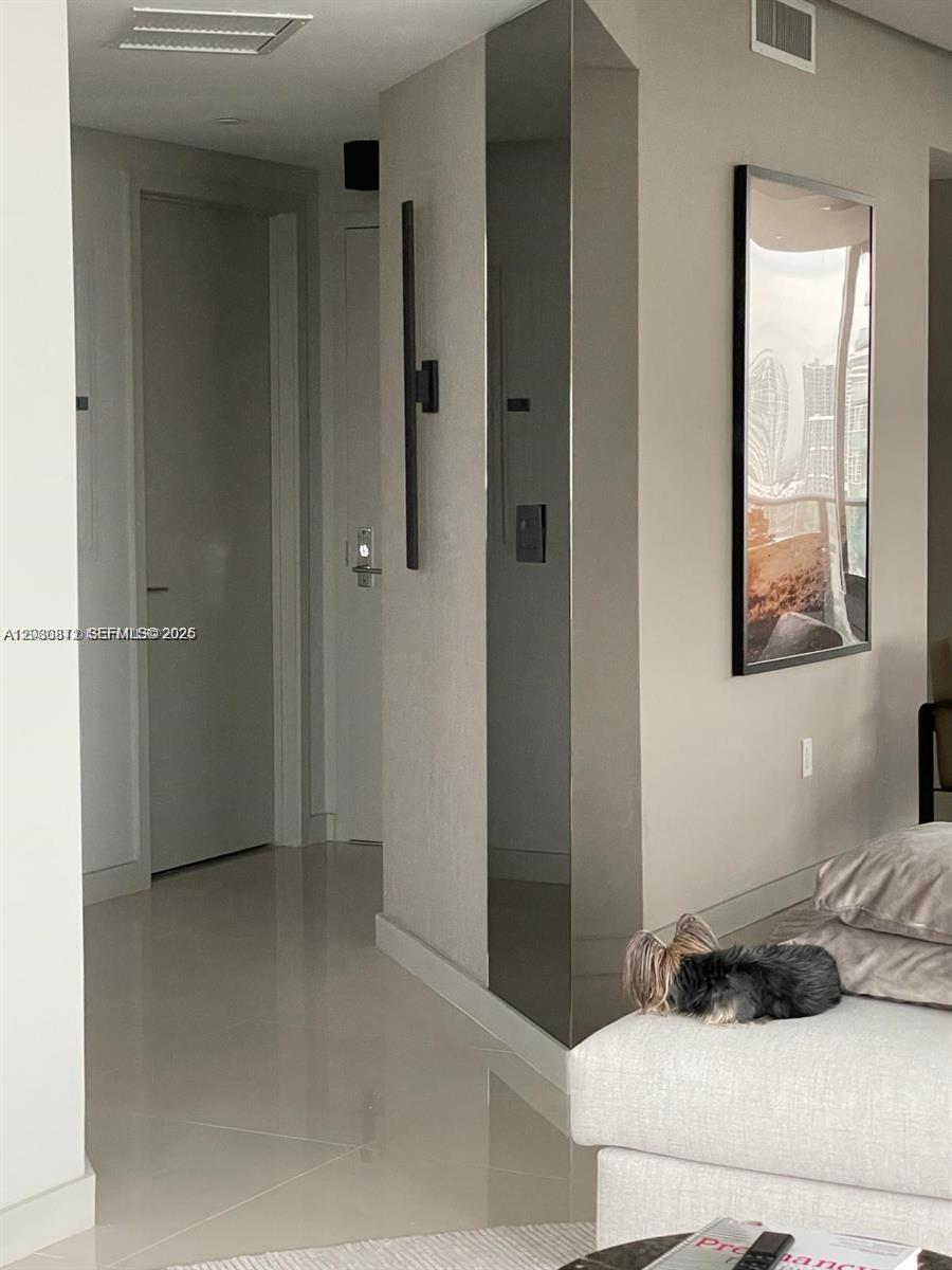 A small dog rests on a sofa near a hallway with a mirrored pillar — 488 NE 18th St # 1901, Miami FL 33132, MIAMI, FL