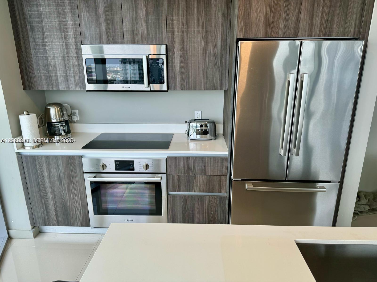 A modern kitchen features wood-grain cabinetry, stainless steel appliances, and white countertops — 488 NE 18th St # 1901, Miami FL 33132, MIAMI, FL