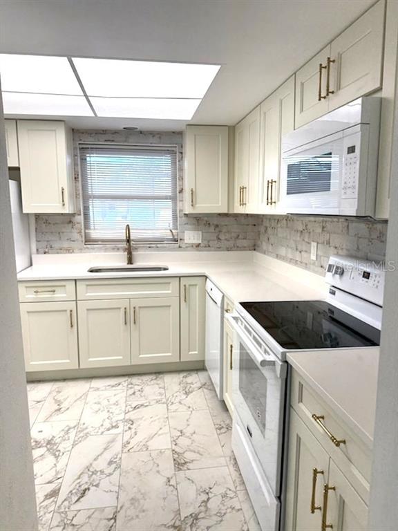 A kitchen features white cabinets, gold hardware, a brick backsplash, and marble-patterned tile flooring — 610 INDIAN ROCKS ROAD N UNIT 103, BELLEAIR BLUFFS, FL