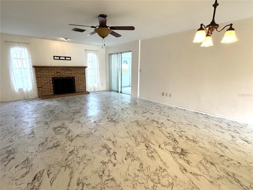 A living room features marble-look tile flooring, a brick fireplace, and a ceiling fan — 610 INDIAN ROCKS ROAD N UNIT 103, BELLEAIR BLUFFS, FL