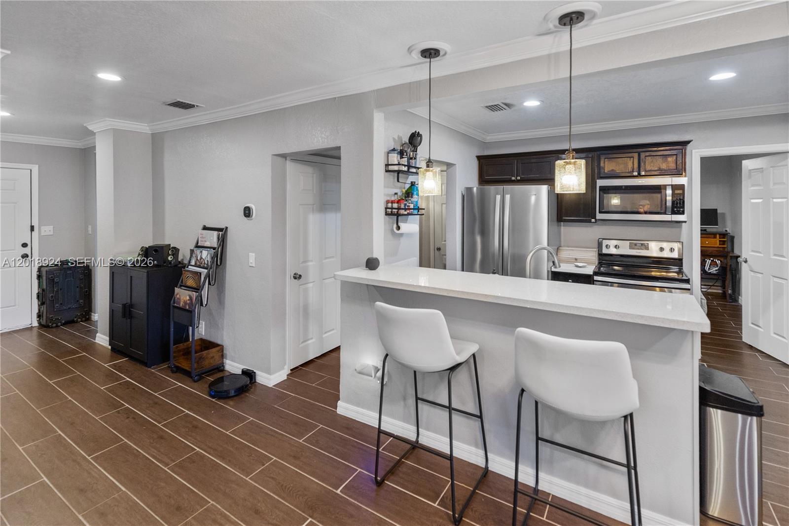 A kitchen features a white breakfast bar, two stools, dark cabinetry, and wood-look tile flooring — ORLANDO, FL