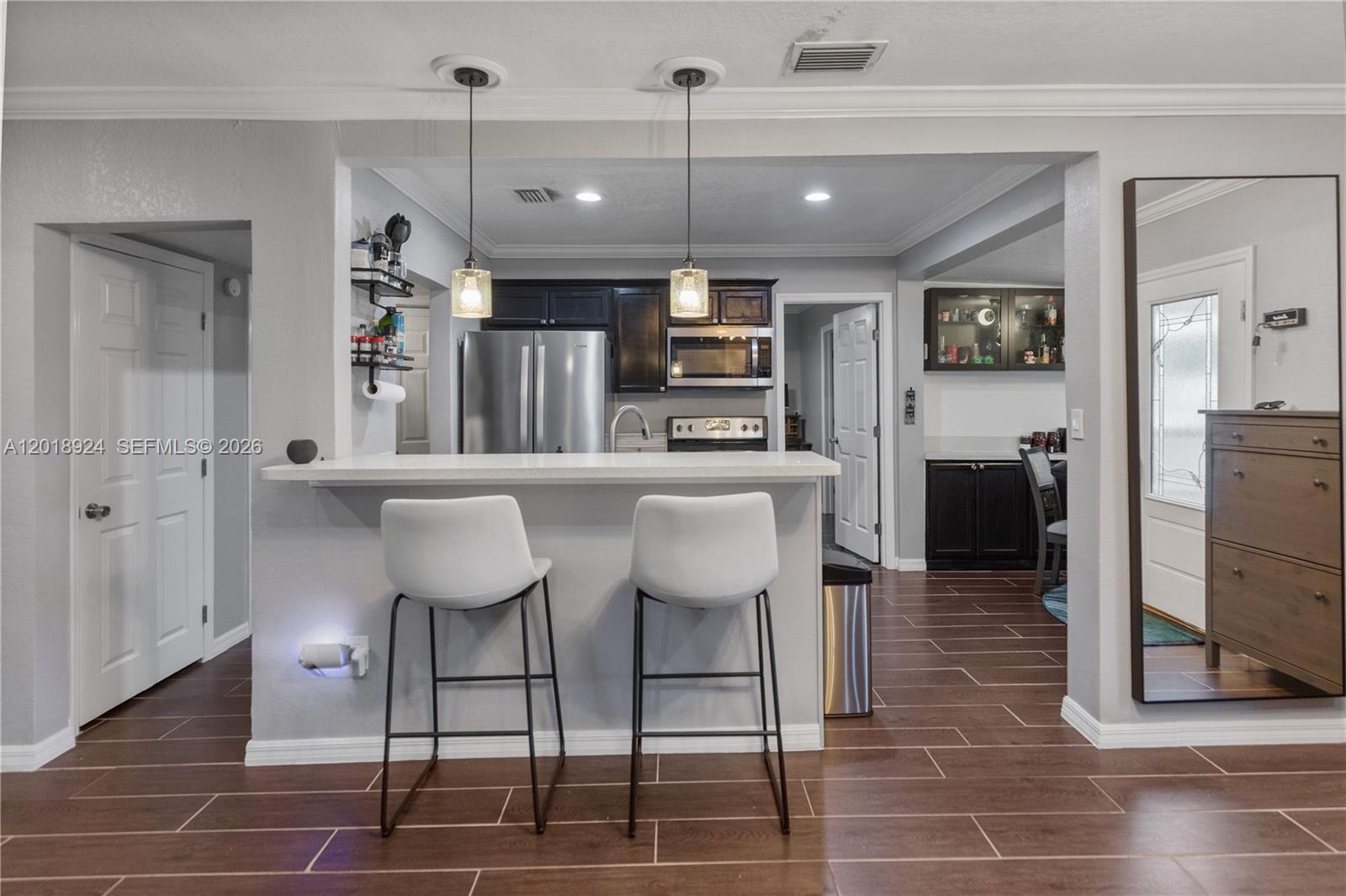 A kitchen with a breakfast bar, two stools, dark cabinets, and wood-look tile flooring — ORLANDO, FL