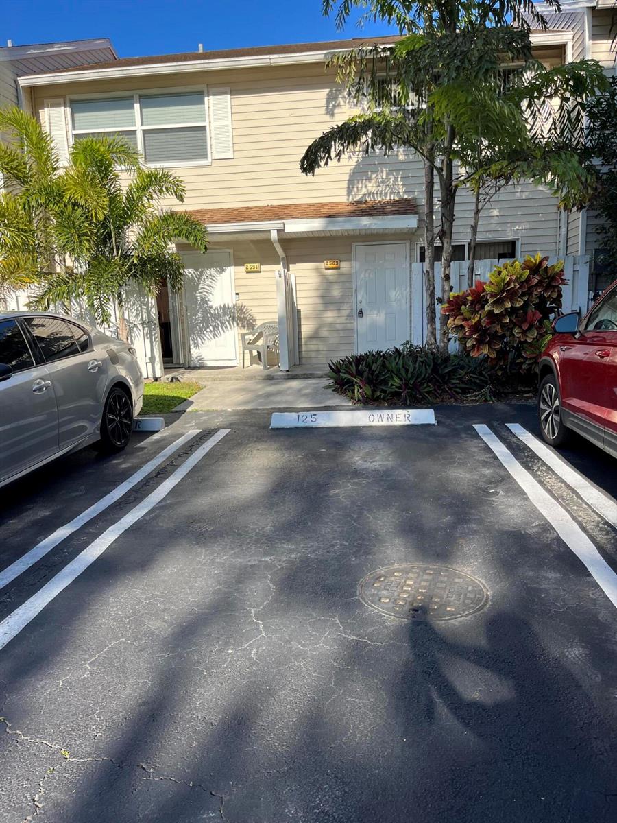 A two-story townhouse exterior features beige siding, two white doors, and a reserved parking space — 2589 NE 15th Street, Pompano Beach FL 33062, POMPANO BEACH, FL