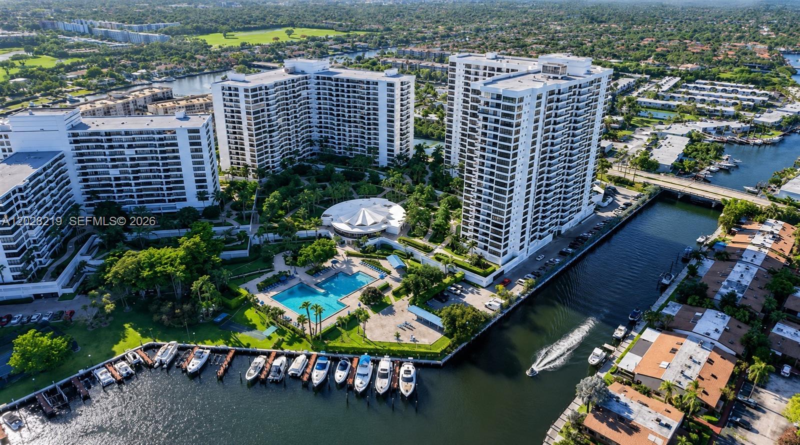 An aerial view shows several high-rise apartment buildings, a swimming pool, and boats docked along a canal — 2500 Parkview Dr # 1815, Hallandale Beach FL 33009, HALLANDALE BEACH, FL