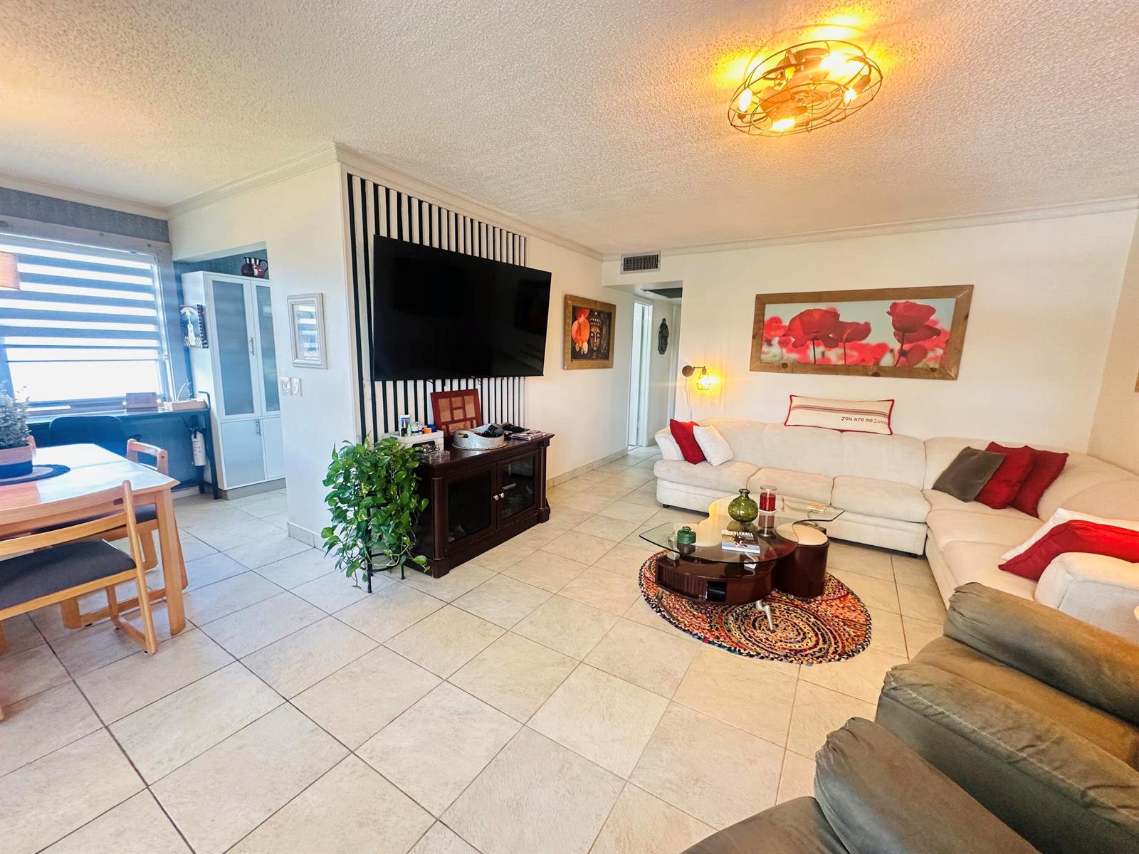 A living room features a striped accent wall with a television, tile flooring, and sectional — 200 Ventnor L # 200, Deerfield Beach FL 33442, DEERFIELD BEACH, FL