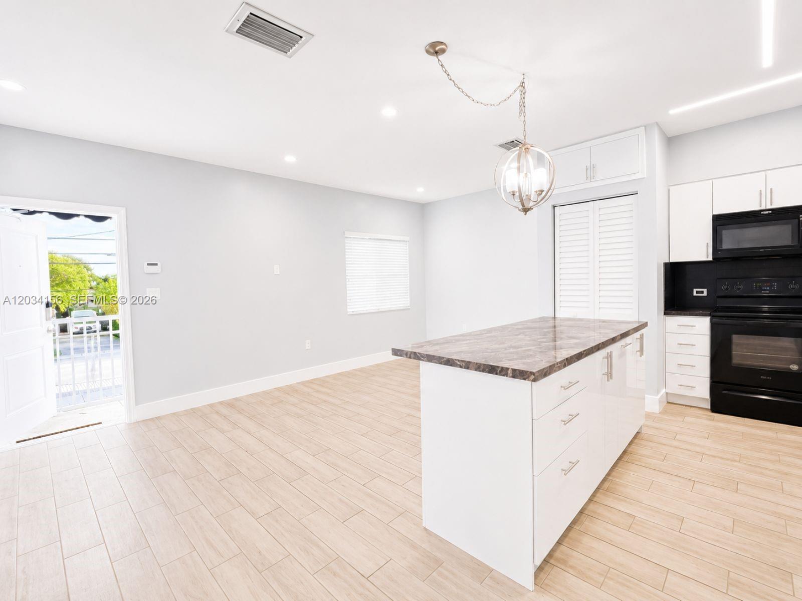 A kitchen features a marble-topped island, white cabinetry, black appliances, and light wood-look flooring — 7135 SW 21st St # 1, Miami FL 33155, MIAMI, FL