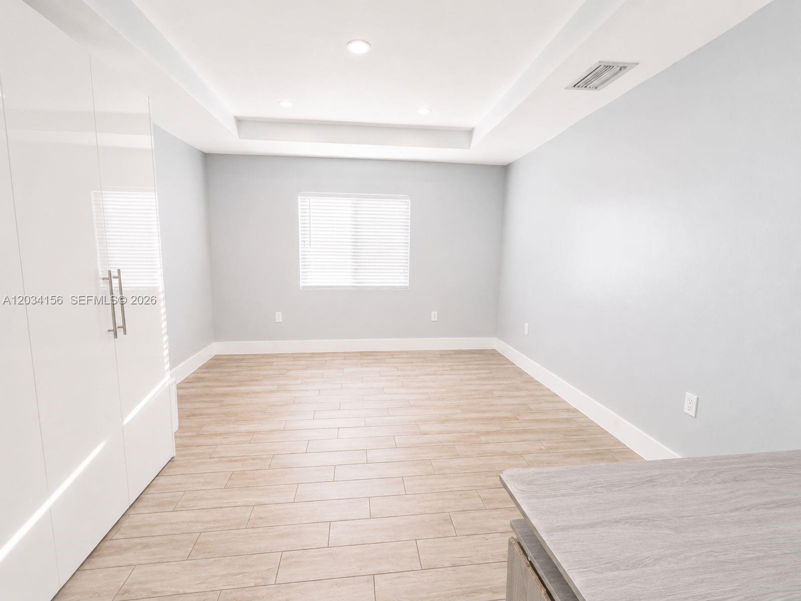 A room with light-colored wood-look tile flooring, white walls, a tray ceiling, and white cabinetry — 7135 SW 21st St # 1, Miami FL 33155, MIAMI, FL