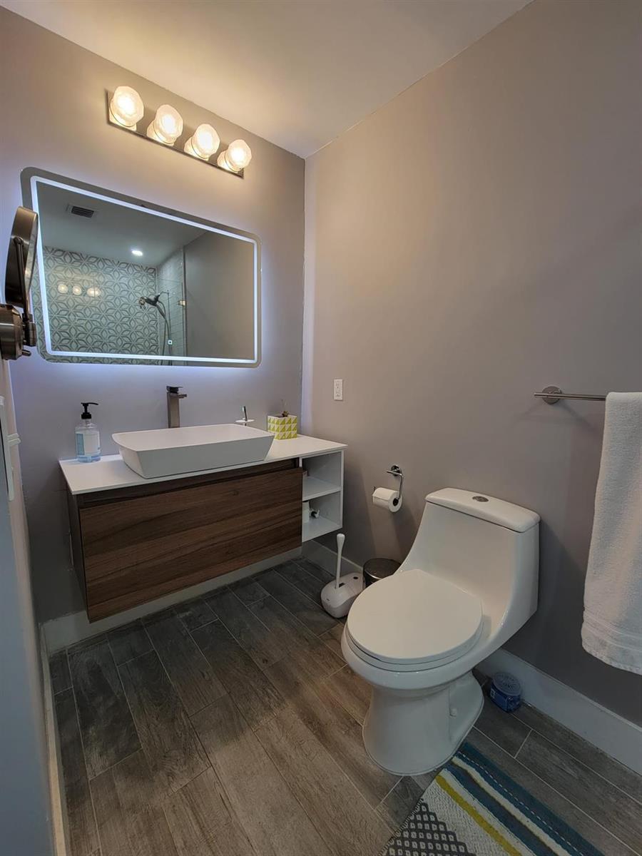 A modern bathroom features a floating wood vanity, vessel sink, illuminated mirror, and white toilet — OAKLAND PARK, FL