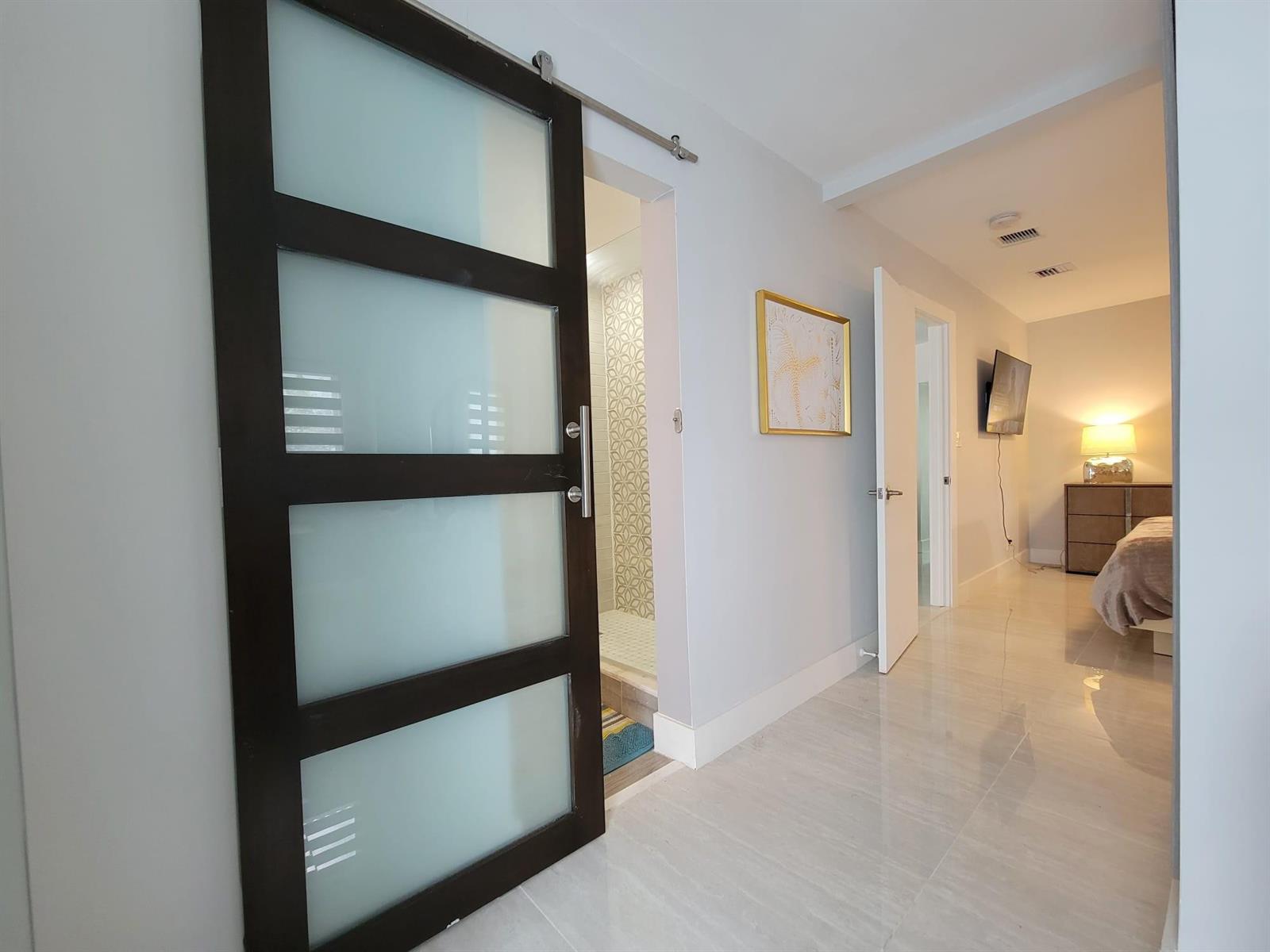 A hallway features a dark wood sliding barn door with frosted glass panels and tile flooring — OAKLAND PARK, FL