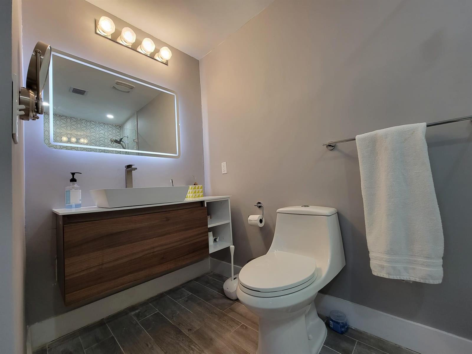 A modern bathroom features a floating wood vanity, vessel sink, LED mirror, and white toilet — OAKLAND PARK, FL