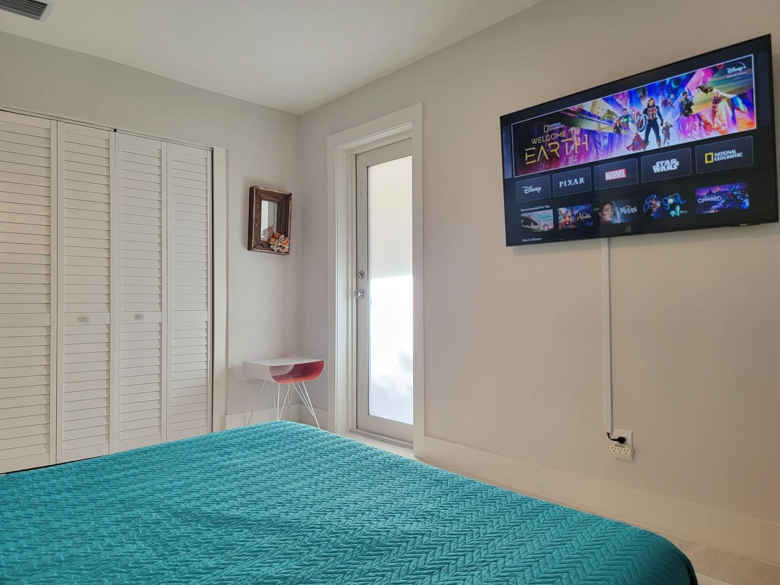 A bedroom features a teal bed, a wall-mounted television, and a glass-paneled door — OAKLAND PARK, FL
