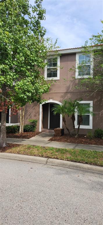 A two-story townhouse exterior with a brown stucco facade, arched entryway, and surrounding landscaping — 4546 ALBERTO CIRCLE, KISSIMMEE, FL