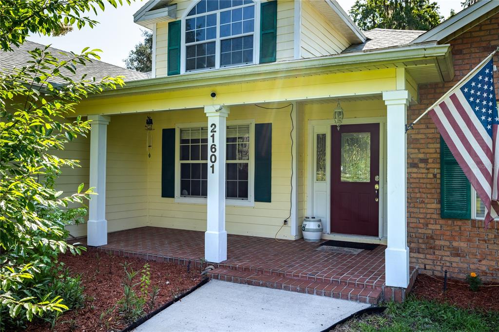 A front porch with brick flooring, white columns, and a red door on a yellow house — 21601 OLD BELLAMY ROAD, ALACHUA, FL