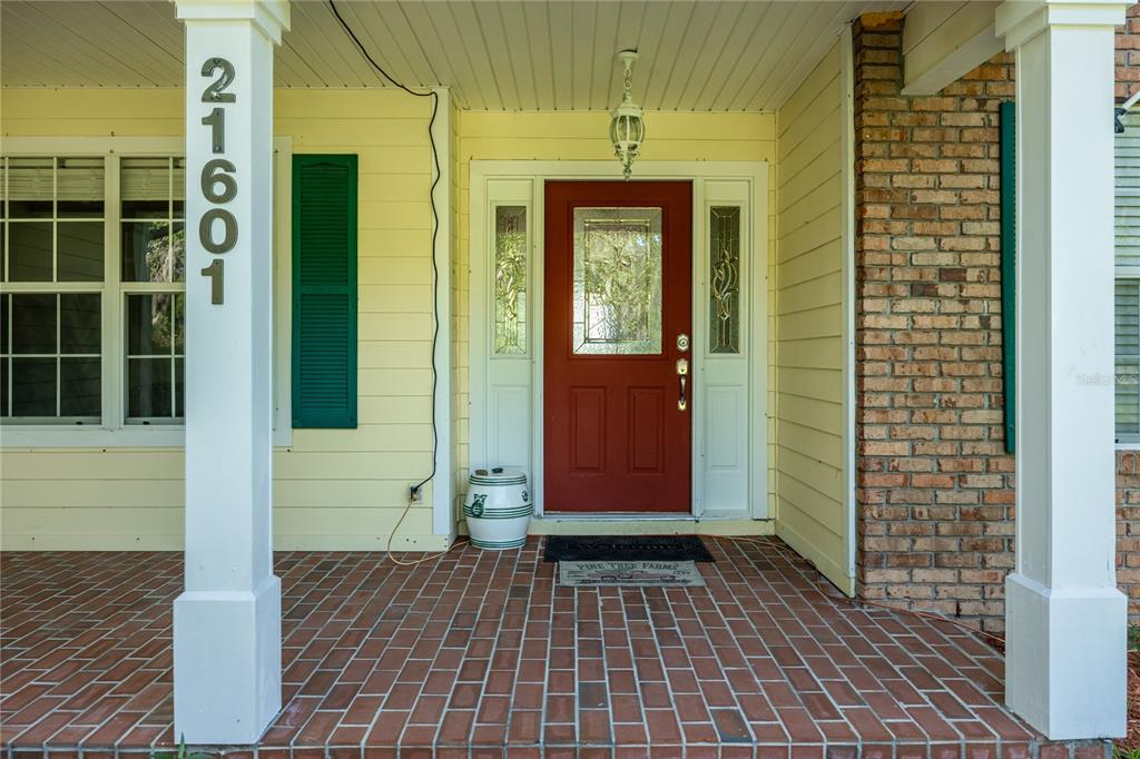 A front porch with a red door, brick flooring, and a white column with house numbers — 21601 OLD BELLAMY ROAD, ALACHUA, FL