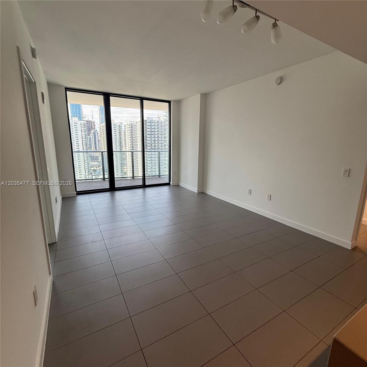 An empty living room features large floor-to-ceiling windows, gray tile flooring, and white walls — 1600 NE 1st Ave # 2607, Miami FL 33132, MIAMI, FL