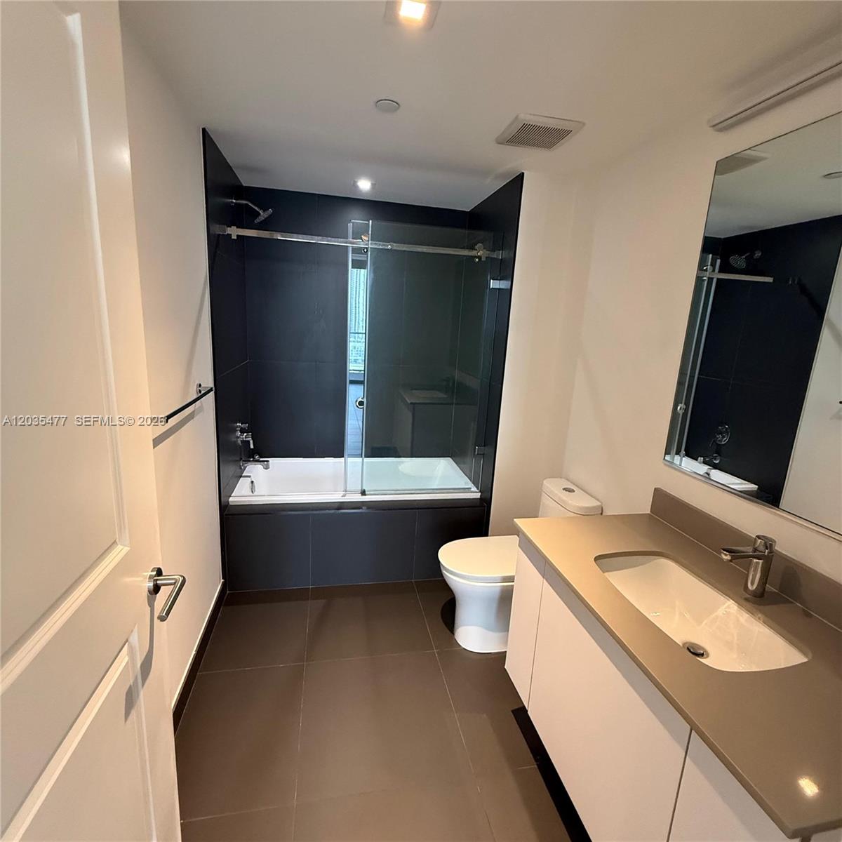 A modern bathroom features a dark-tiled shower-tub combo, a white vanity, and a toilet — 1600 NE 1st Ave # 2607, Miami FL 33132, MIAMI, FL