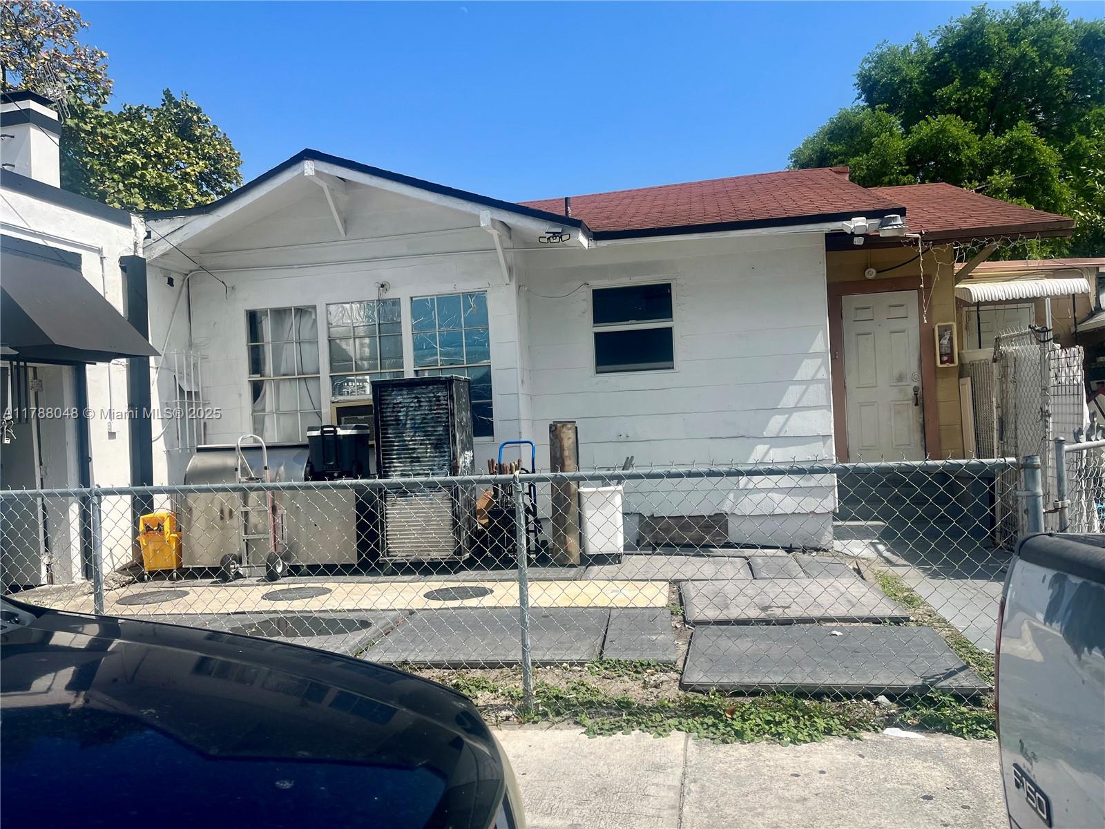 A white single-story house exterior features a red roof, chain-link fence, and paved patio area — 1574 SW 1st St, Miami FL 33135, MIAMI, FL
