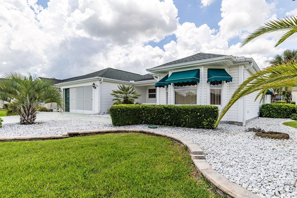 A white house with a green awning, a palm tree, and a rock-covered front yard — 814 SANTA RITA WAY, THE VILLAGES, FL