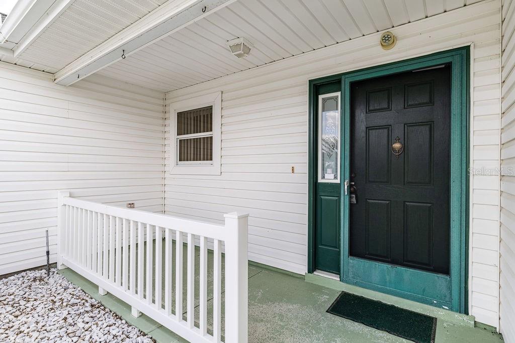 A covered porch features white siding, a green floor, a white railing, and a black door — 814 SANTA RITA WAY, THE VILLAGES, FL