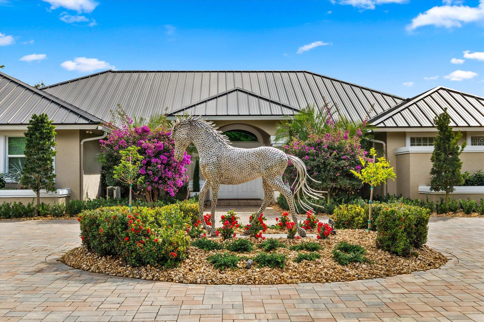 A metal horse sculpture stands in a circular garden bed in front of a house — 14868 Paddock Drive, Wellington FL 33414, WELLINGTON, FL