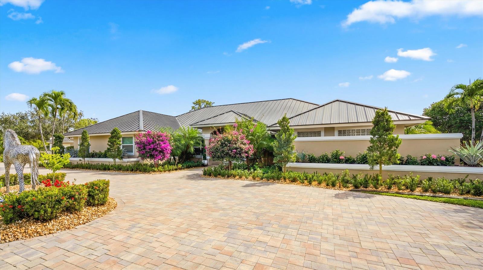 A paved driveway leads to the front entrance of a tan house with a metal roof — 14868 Paddock Drive, Wellington FL 33414, WELLINGTON, FL