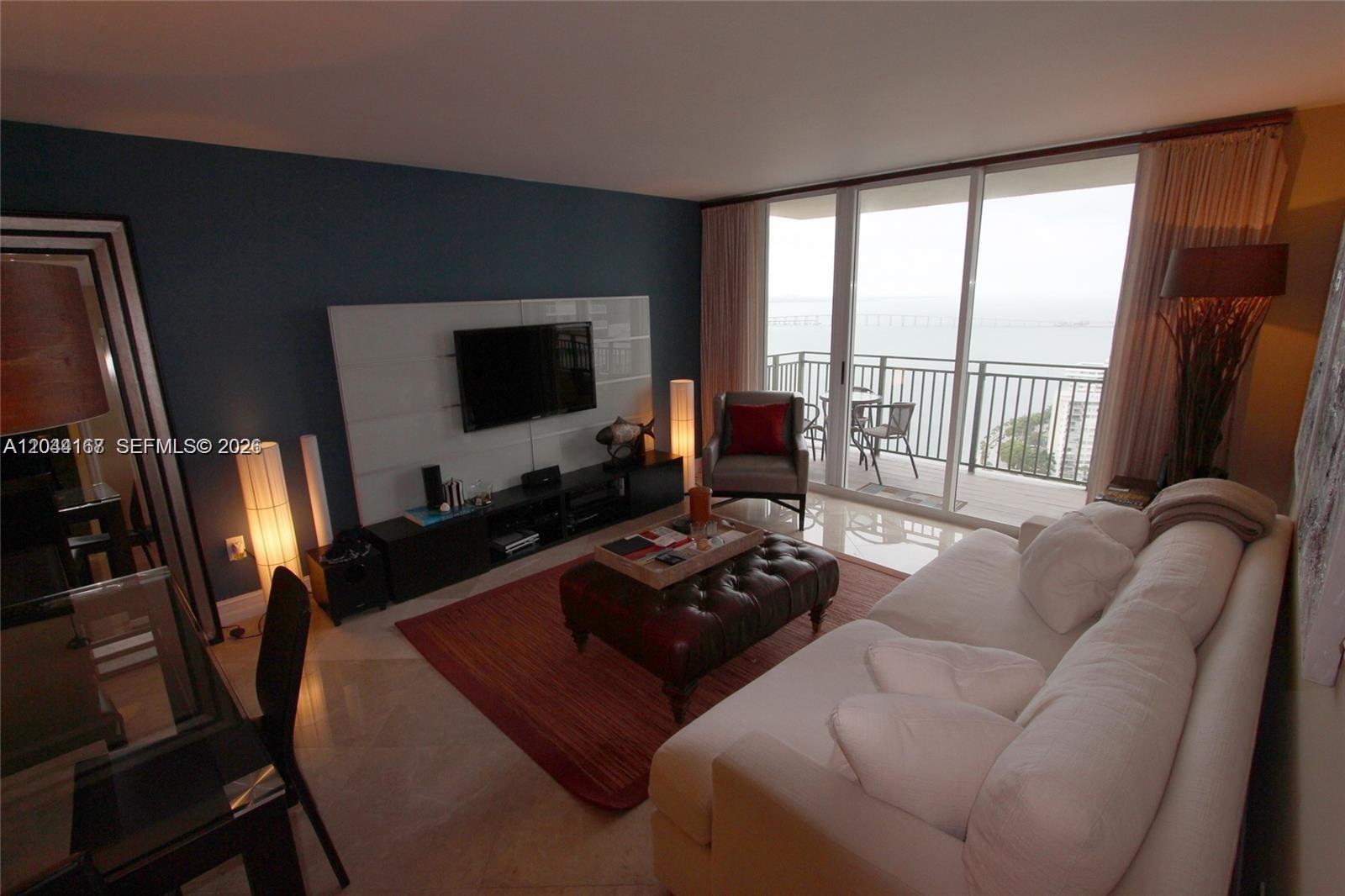 A living room features a white sofa, leather ottoman, and a balcony overlooking the water — 1155 Brickell Bay Dr # 3107, Miami FL 33131, MIAMI, FL