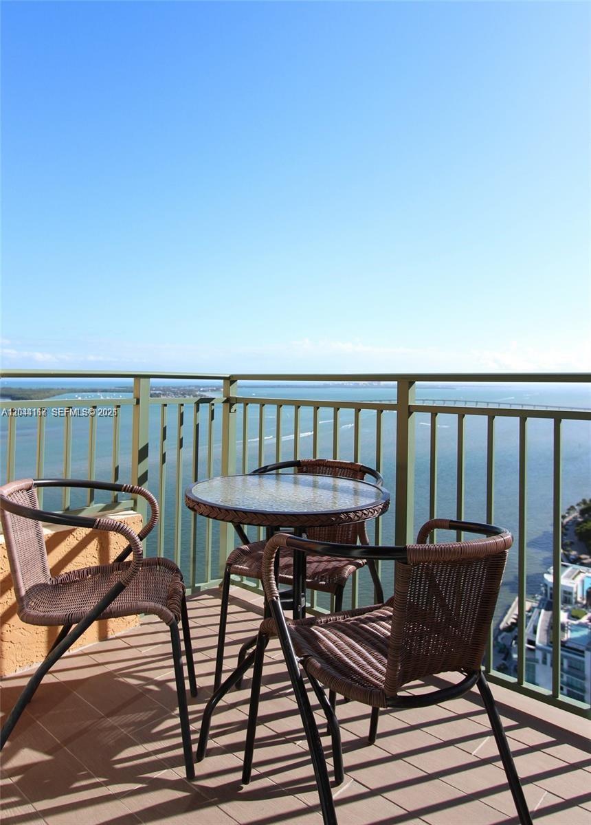 A balcony features a small round table and three wicker chairs overlooking the ocean — 1155 Brickell Bay Dr # 3107, Miami FL 33131, MIAMI, FL