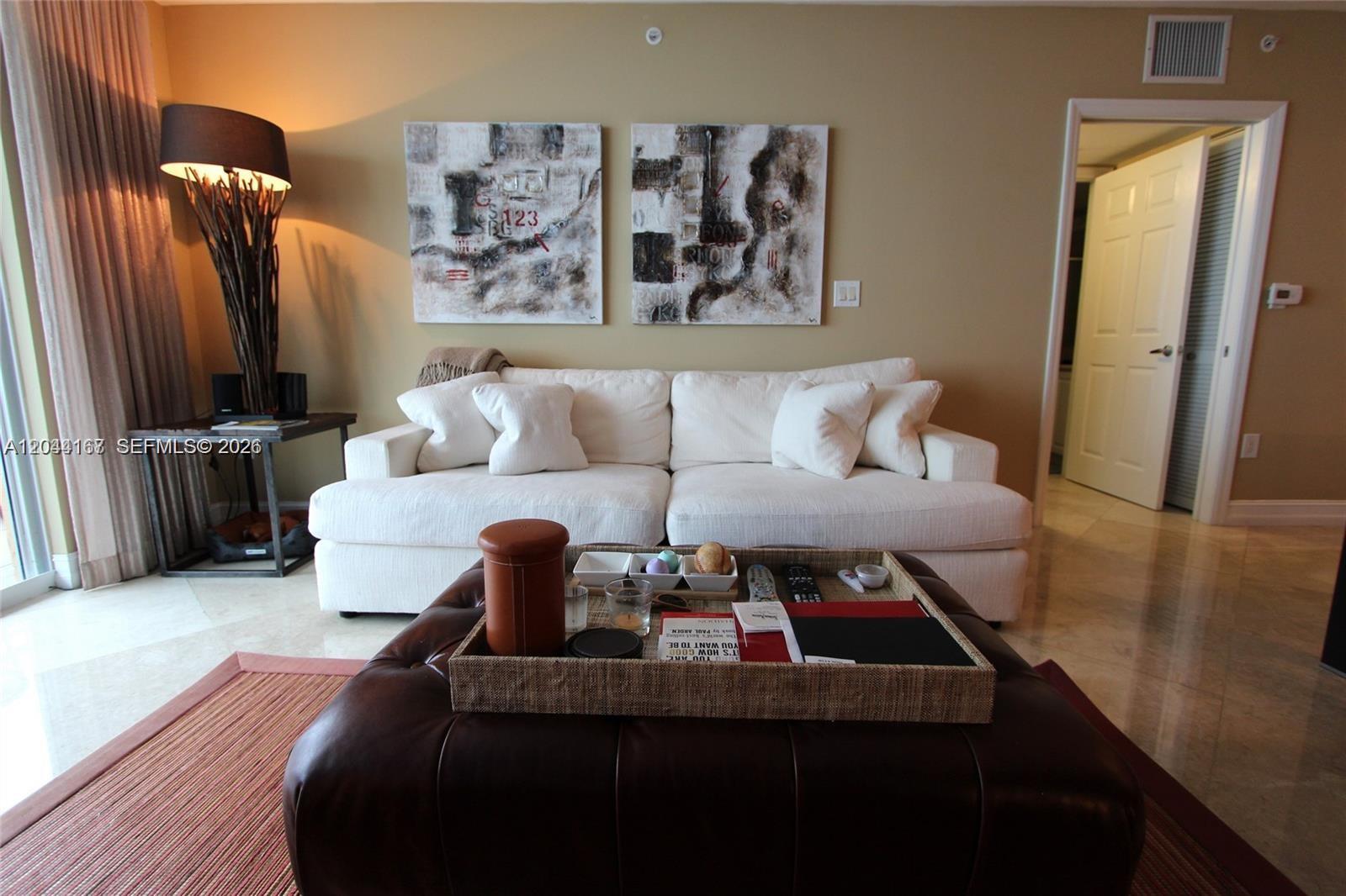 A living room features a white sofa, a leather ottoman, and two abstract wall paintings — 1155 Brickell Bay Dr # 3107, Miami FL 33131, MIAMI, FL