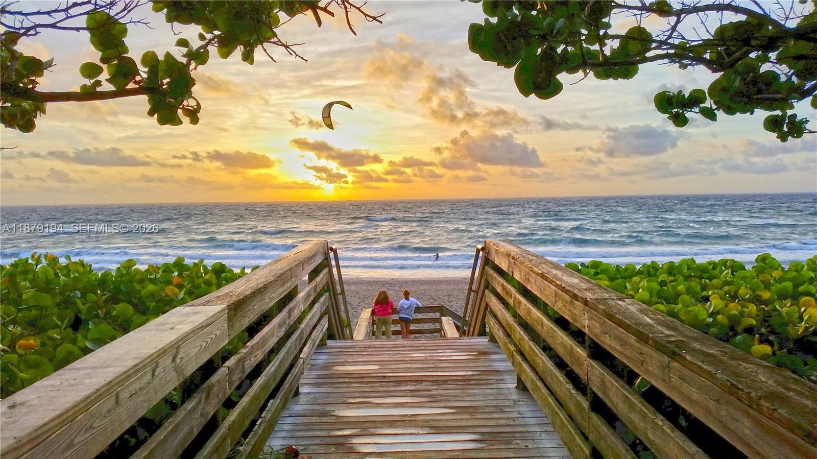 A wooden boardwalk leads to a sandy beach at sunset with two people standing ahead — 1801 Mainsail Cir # 1801, Jupiter FL 33477, JUPITER, FL