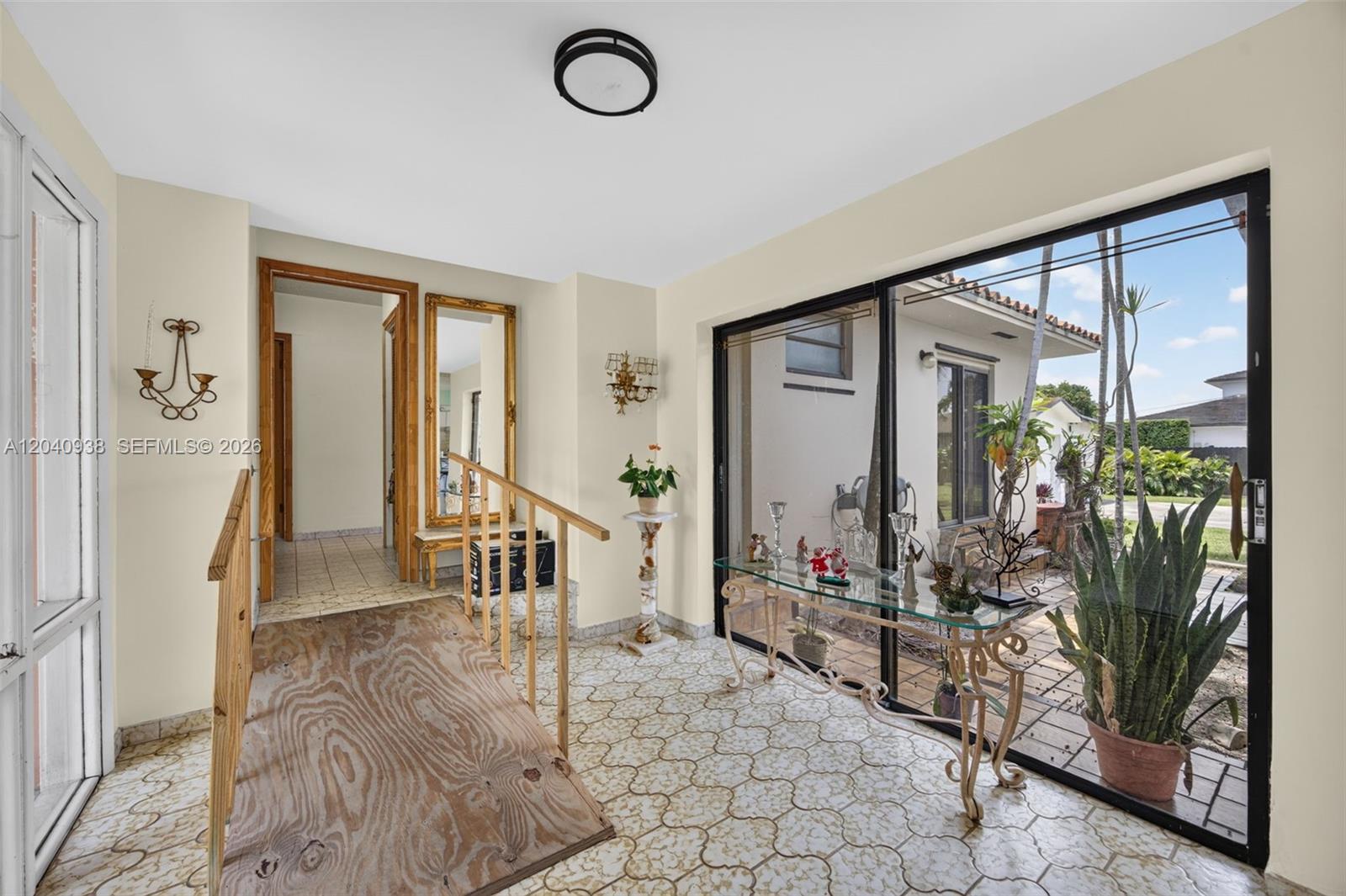 A sunroom features a wooden ramp, tiled flooring, a glass console table, and sliding doors — 11405 SW 32nd St, Miami FL 33165, MIAMI, FL