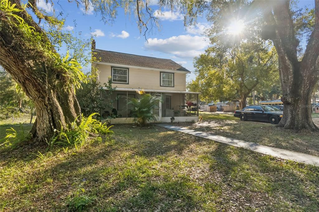 A two-story house with light siding and a screened-in porch sits between two large trees — 19222 FORT DADE AVENUE, BROOKSVILLE, FL