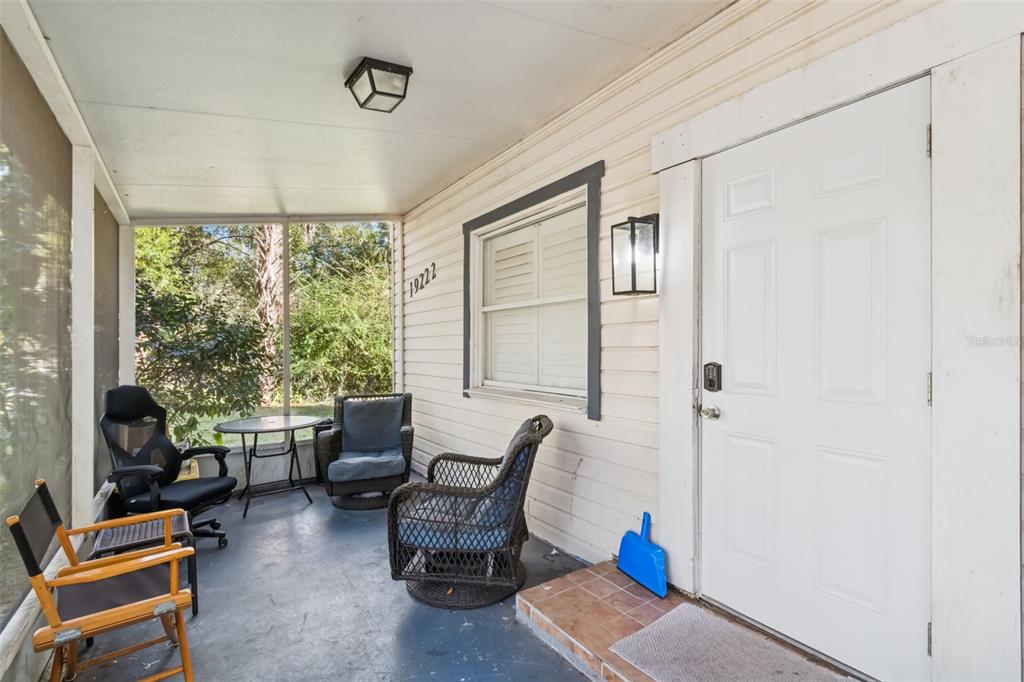 A screened-in porch features a white door, several chairs, a small table, and siding — 19222 FORT DADE AVENUE, BROOKSVILLE, FL