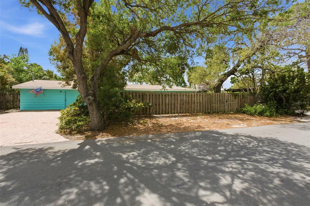 A turquoise house with a brick driveway and a wooden fence sits behind large trees — 528 RALPH STREET, SARASOTA, FL