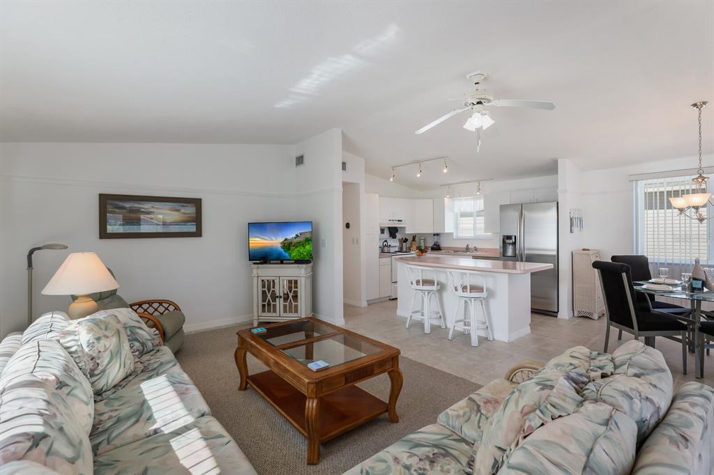 An open-concept living room and kitchen featuring floral sofas, a wooden coffee table, and island — 2804 AVENUE C, HOLMES BEACH, FL