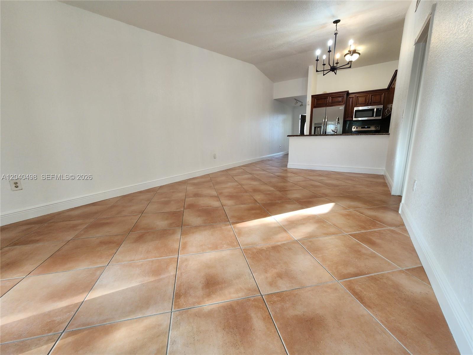 An open-concept room features diagonal tan floor tiles, white walls, and a kitchen area — 13412 SW 17th Terr Cir S, Miami FL 33175, MIAMI, FL