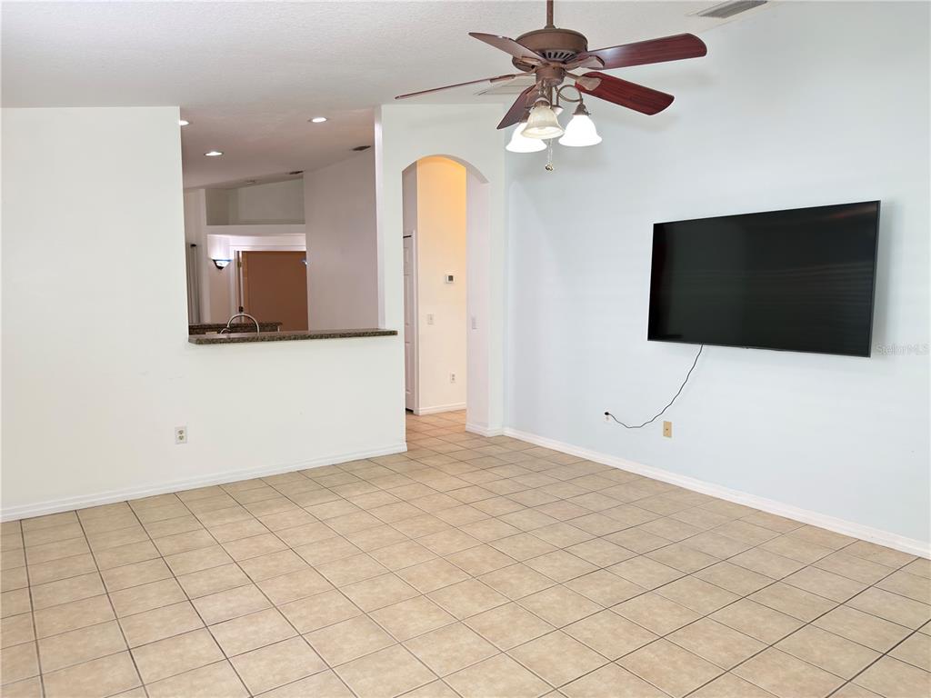 An open living room features tile flooring, a ceiling fan, and a wall-mounted television — 414 ULELAH AVENUE, PALM HARBOR, FL