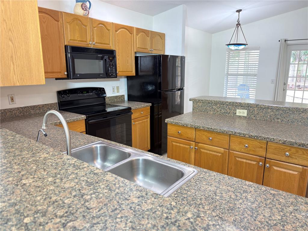 A kitchen features oak cabinets, black appliances, and speckled granite countertops — 414 ULELAH AVENUE, PALM HARBOR, FL