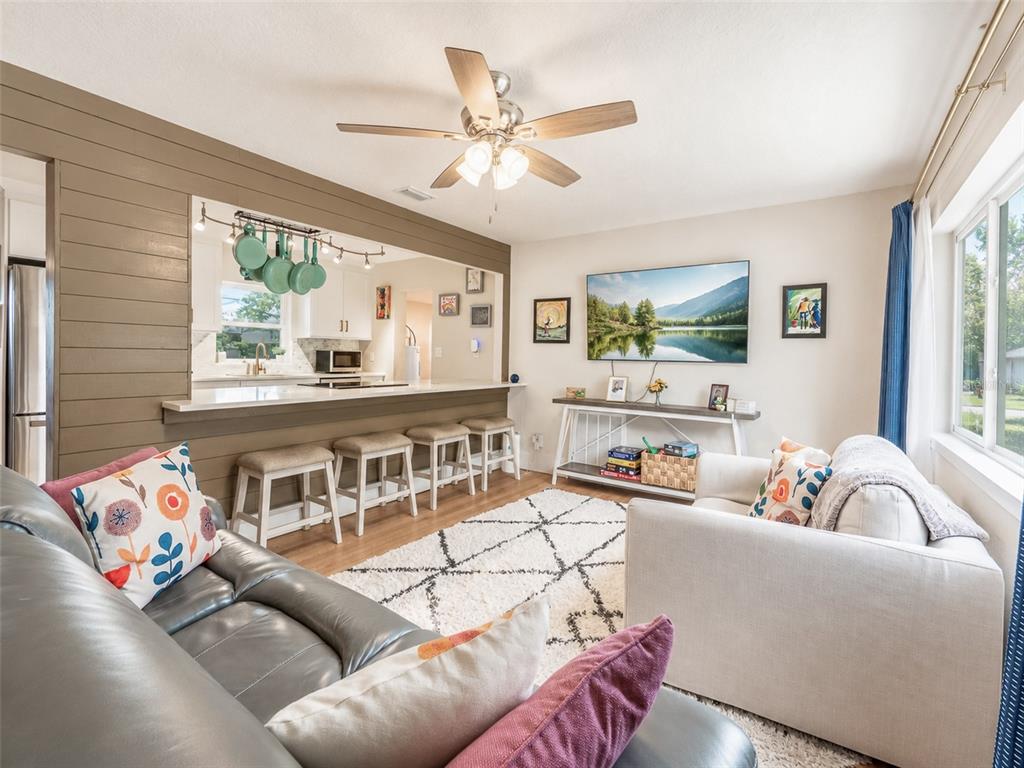 A living room with a gray sofa, white armchair, breakfast bar, and wood-paneled accent wall — 304 E JERSEY STREET, ORLANDO, FL