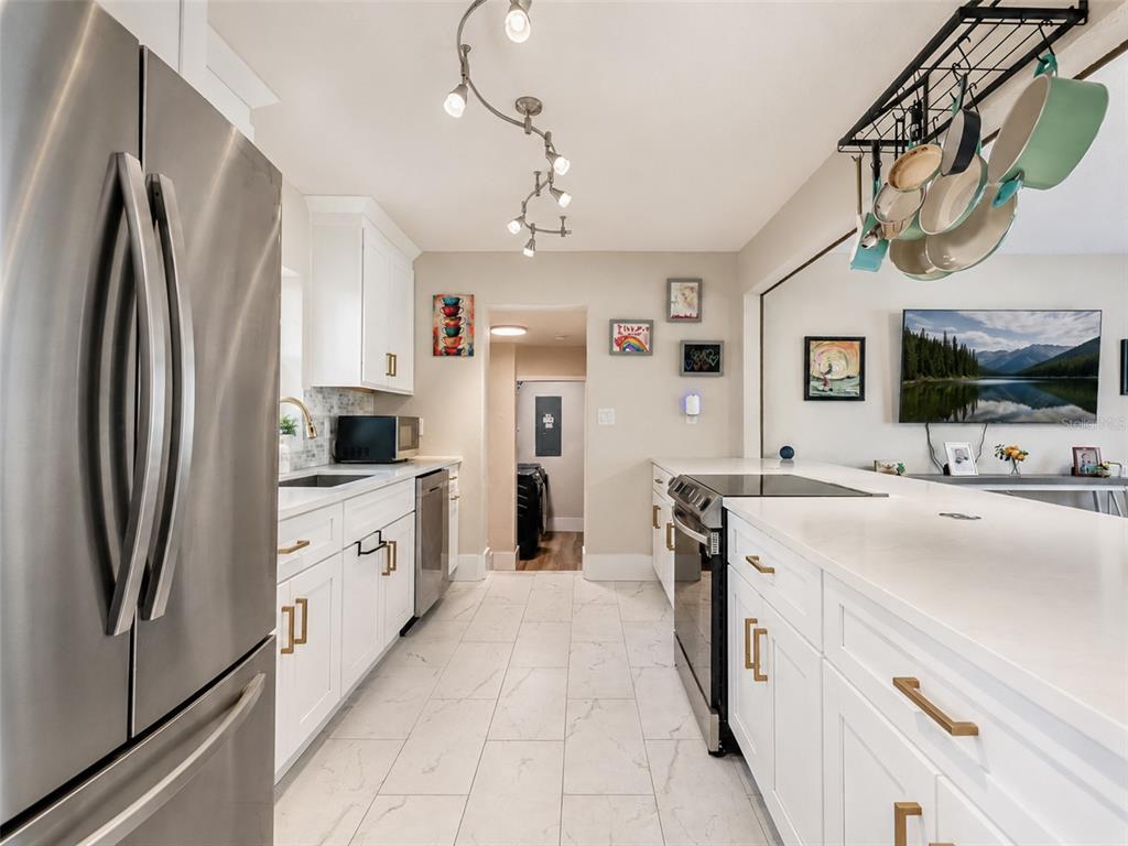 A bright kitchen features white cabinets, stainless steel appliances, quartz countertops, and a hanging pot rack — 304 E JERSEY STREET, ORLANDO, FL