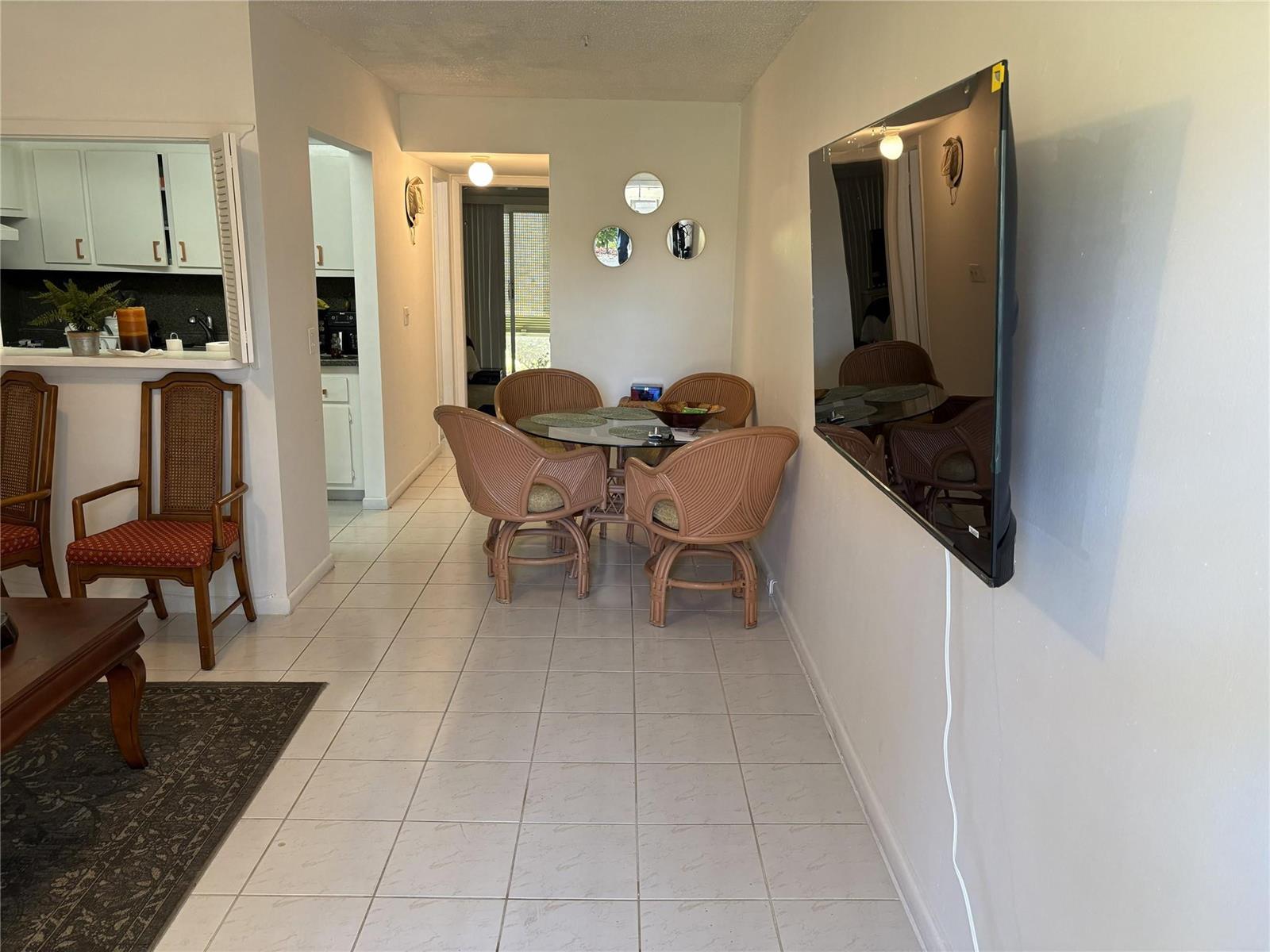 A dining area with a glass table and wicker chairs sits near a wall-mounted television — 91 Preston C # C, Boca Raton FL 33434, BOCA RATON, FL