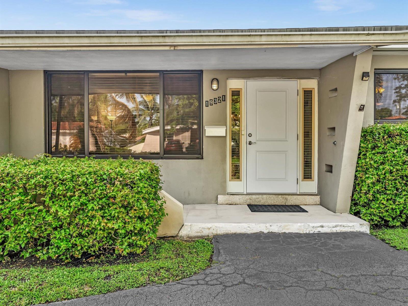 The exterior of a house features a white front door, a large window, and landscaping — 19321 NE 18th Place, Miami FL 33179, MIAMI, FL
