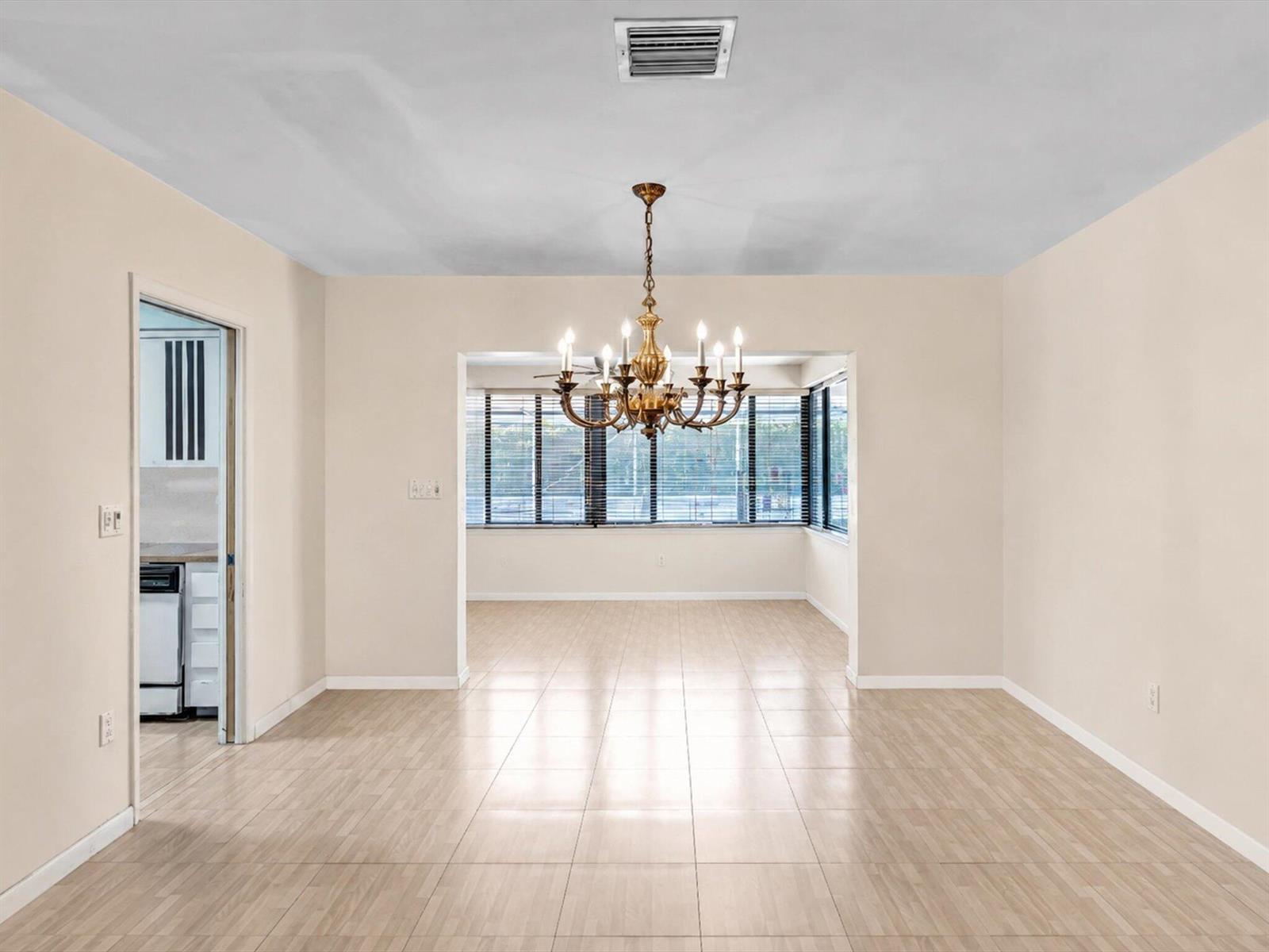 A dining room with light-colored tile flooring, a brass chandelier, and an adjacent kitchen doorway — 19321 NE 18th Place, Miami FL 33179, MIAMI, FL